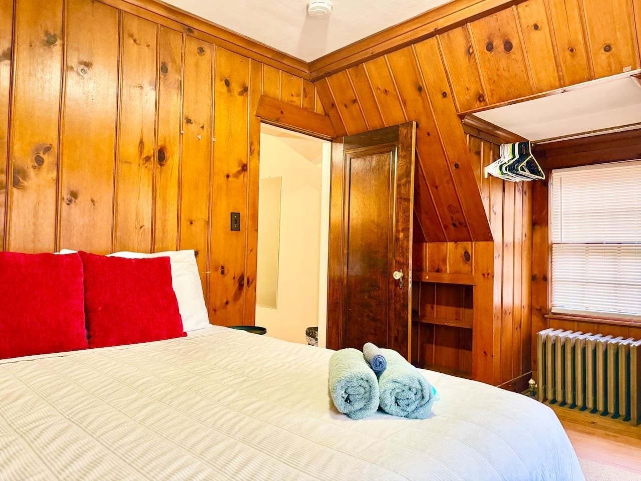 Een kamer met houten lambrisering, een bed, rode en witte kussens, en opgerolde handdoeken.