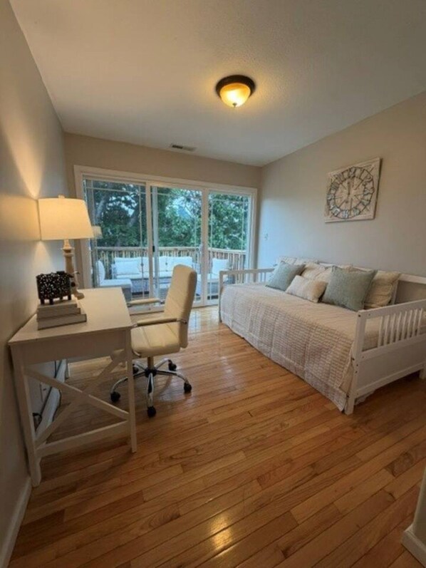 A room with a white desk, chair, and bed, a ceiling light, and a window with a view of trees.