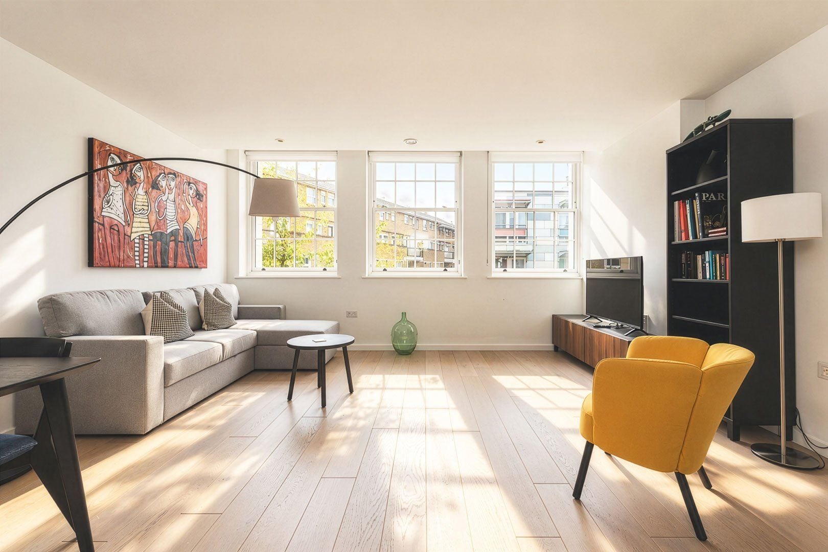 Un salon moderne avec un canapé, un fauteuil jaune, une table basse et une bibliothèque.