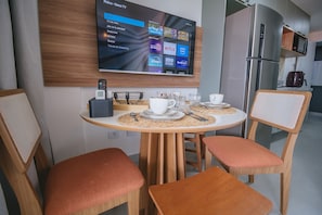 A modern dining area with a round table, two chairs, and a mounted TV displaying streaming services. - Nixxus 316 (Ipojuca)