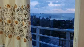 A balcony with a view of the sea and a patterned curtain.