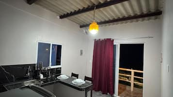 A kitchen with a dining area, a red curtain, and a balcony door.