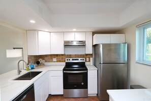 Una cocina compacta con gabinetes blancos, un refrigerador de acero inoxidable, horno empotrado y lavavajillas.