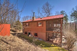 A two-story wooden cabin with a metal roof, a chimney, and a large windowed porch area. - Woodsy WV Cabin near Lost River w Deck & Fire Pit! (Mathias)