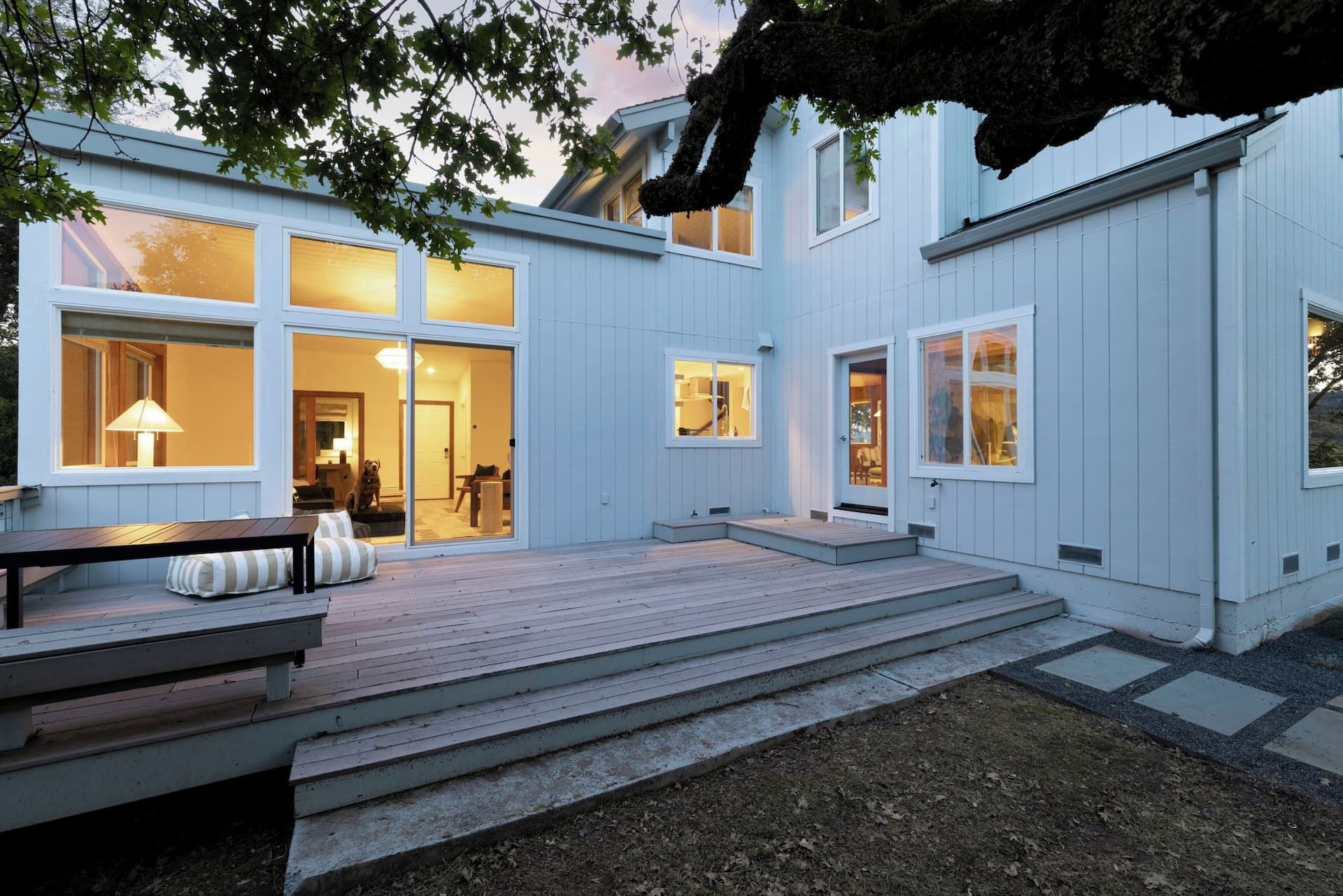 A modern house with large windows, a wooden deck, and a dog visible inside.