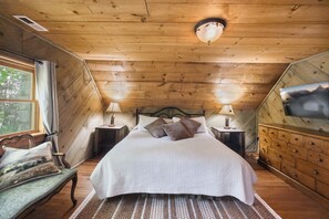 A wooden-paneled bedroom with a bed, two bedside tables, a nightstand, a window with curtains, a wall-mounted TV, and a wooden dresser. - A River Runs Through It- Boone (Vilas)