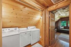 A laundry room with two washing machines and a dryer, wooden walls, and a view of the outdoors through a door. - A River Runs Through It- Boone (Vilas)