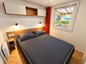 Un dormitorio con cama, mesitas de noche, una ventana con vistas y estanterías empotradas.