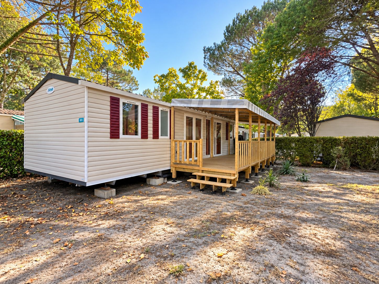 A mobile home with a porch and a small deck, surrounded by trees and a hedge.