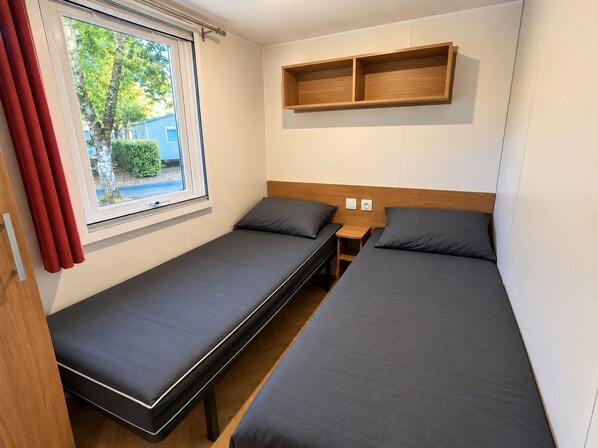 Een kamer met twee eenpersoonsbedden, een raam met gordijnen, een houten hoofdbord en een plank boven de bedden.