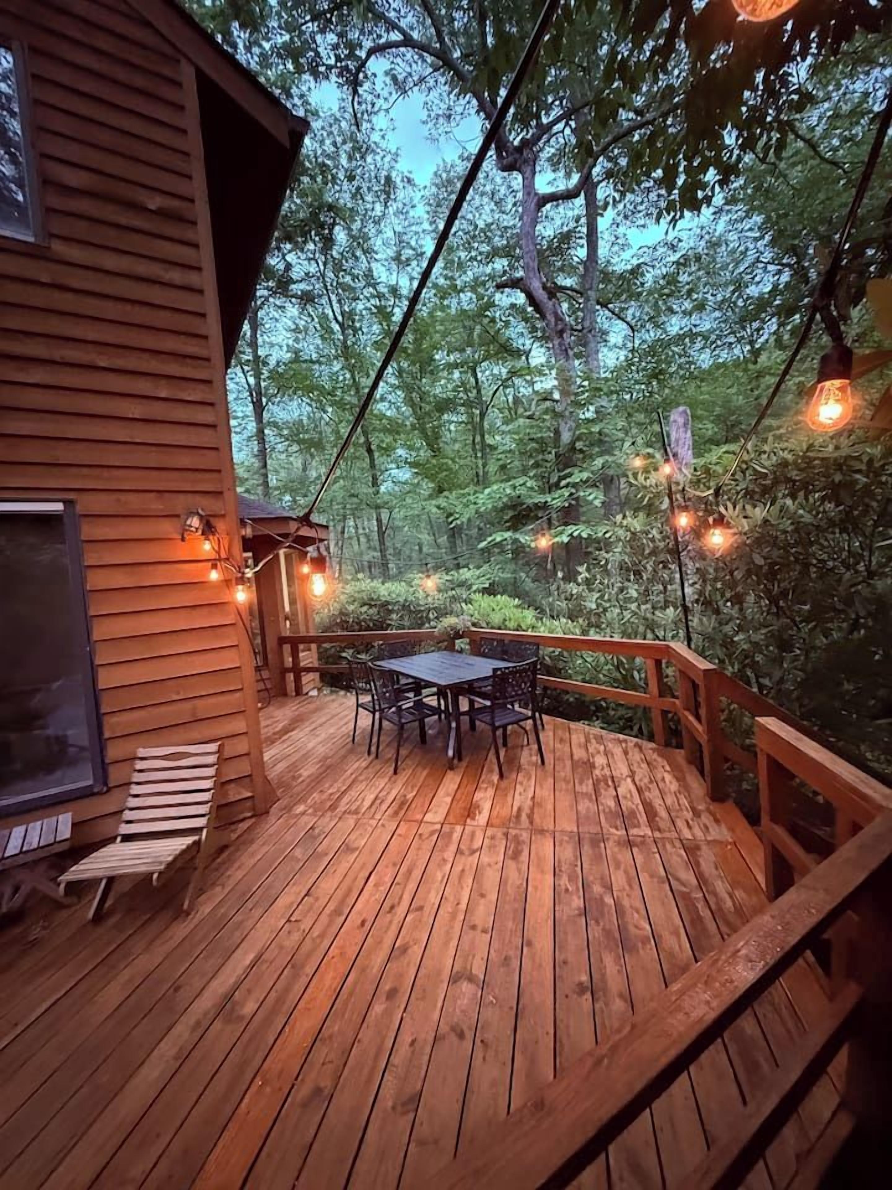 A wooden deck with a table and chairs, surrounded by trees.