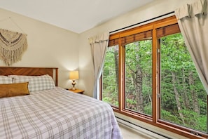 A bedroom with a bed, a bedside lamp, a wall hanging, and a large window with curtains. - "Shanty Springs Retreat" -  Your Creekside Oasis (Banner Elk)