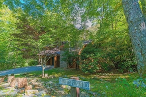 A rustic cabin with a stone exterior, surrounded by lush greenery and a clear road sign indicating 'SHANTY SPRINGS RD.' - "Shanty Springs Retreat" -  Your Creekside Oasis (Banner Elk)
