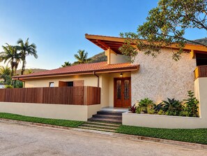 A modern house with a tiled roof, a wooden fence, and a stone wall. - Amore'mare | Charm, Comfort and Sea (Ubatuba)