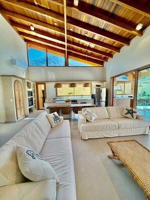 A spacious living area with a high ceiling, a dining area, and a kitchen. - Amore'mare | Charm, Comfort and Sea (Ubatuba)