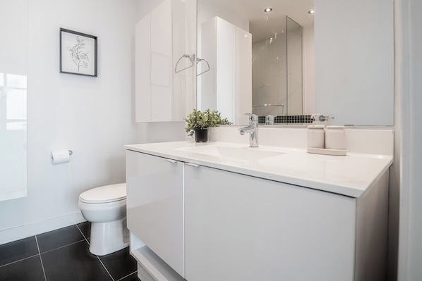 A modern bathroom with a white toilet, a sink with a mirror above it, and a potted plant on the counter. - One-Of-A-Kind Parklawn Penthouse! Unreal Lake View | Parking Available (Toronto)