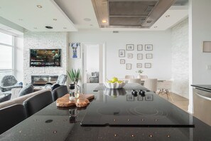 A modern kitchen with a central island, a dining area with a white table, and a living space with a sofa and a TV. - One-Of-A-Kind Parklawn Penthouse! Unreal Lake View | Parking Available (Toronto)
