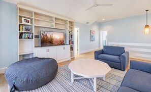 Een moderne woonkamer met een flatscreen televisie, een grijze pluche stoel, een blauwe bank en een witte salontafel.