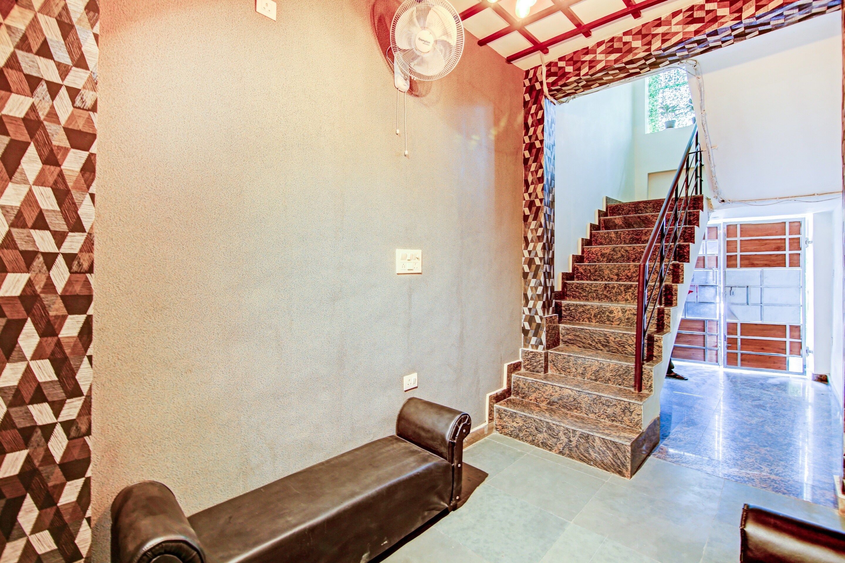 A room with a patterned wall, a bench, a staircase, and a fan.