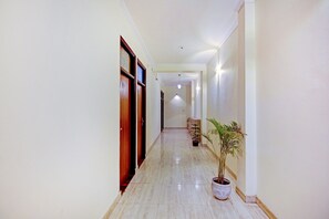 A hallway with wooden doors, a potted plant, and a light fixture. - Hotel O Sky In Near By Sector 62 (Ghaziabad)