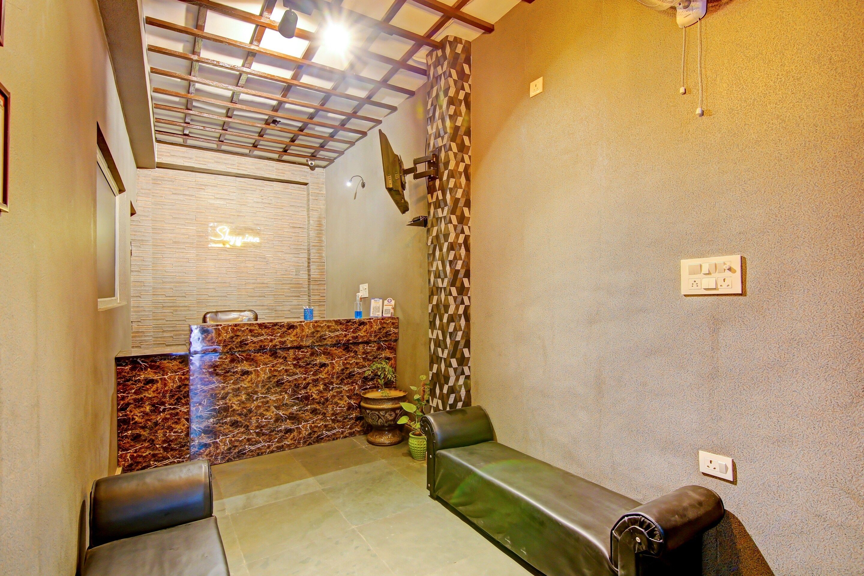 A hotel reception area with a reception desk, a seating area with a sofa, a patterned wall, and a ceiling with a wooden beam structure.