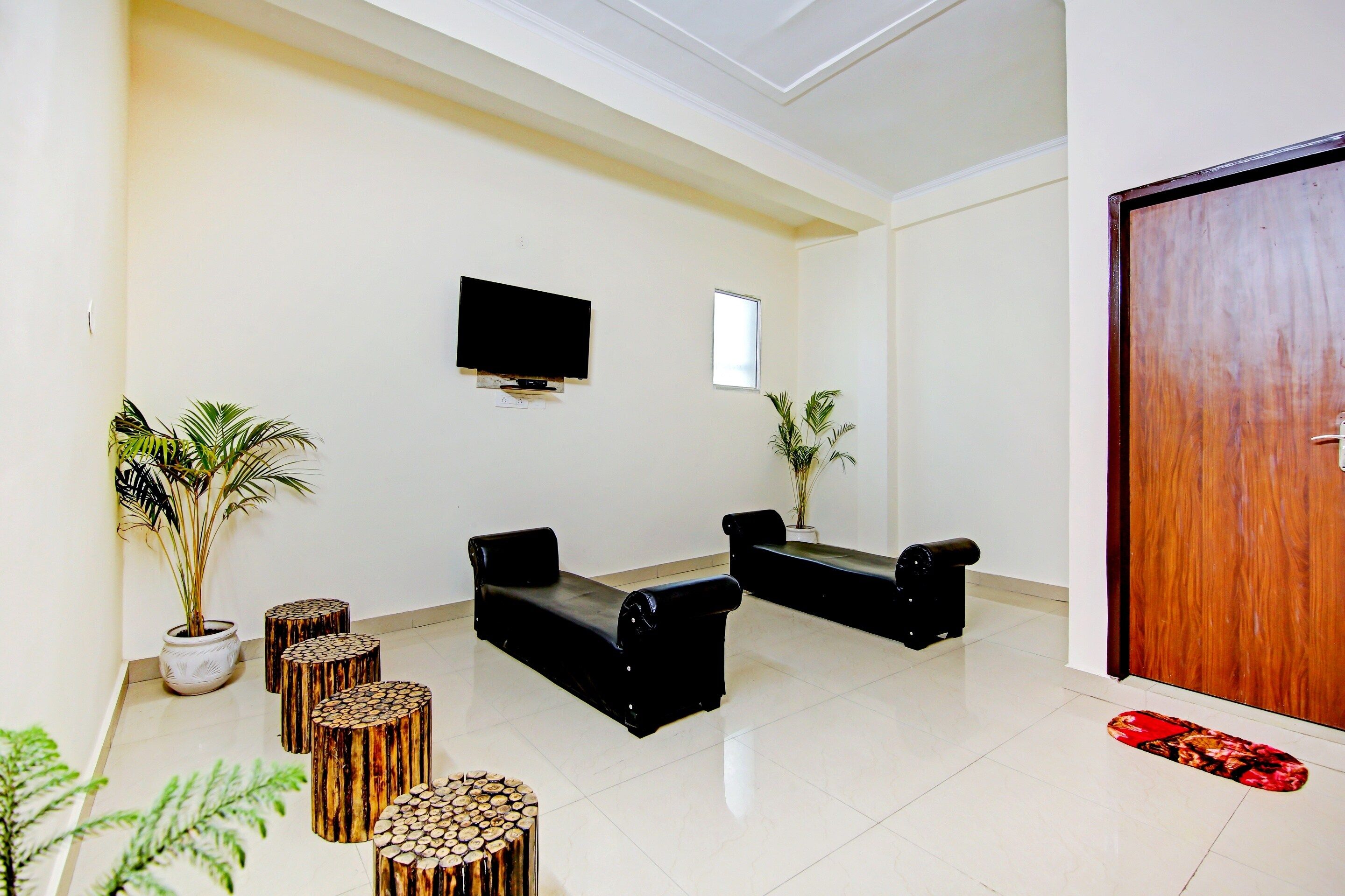 Un área de recepción con un televisor de pantalla plana montado en la pared, dos sofás negros, una mesa de centro de madera y una planta en maceta.