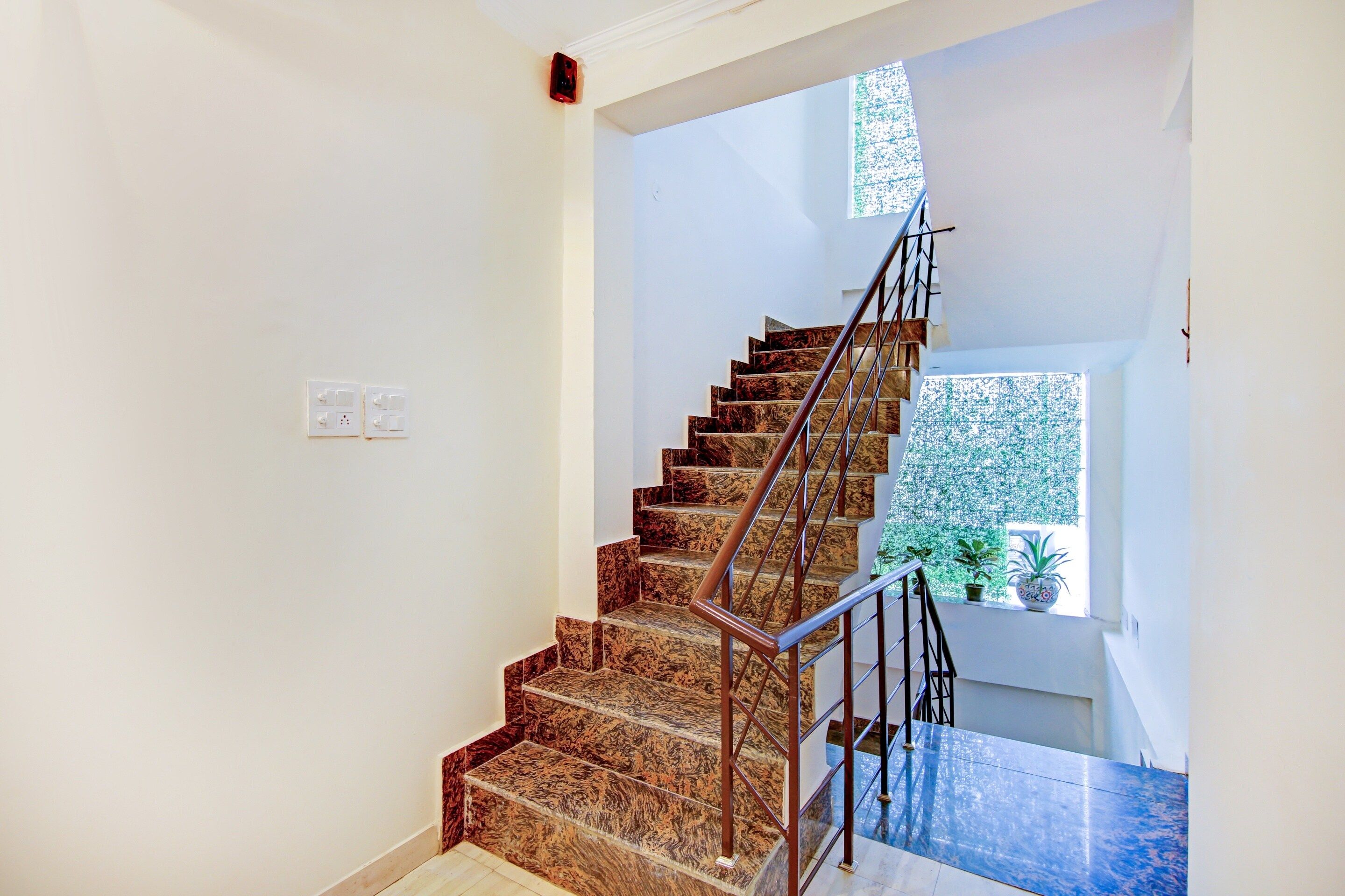 A staircase with marble steps and metal railings, leading to a landing with a window and a potted plant.