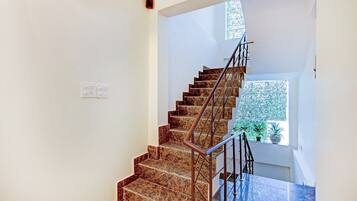 Una escalera con escalones de mármol y barandas de metal que conduce a una plataforma con una ventana y una planta en maceta.