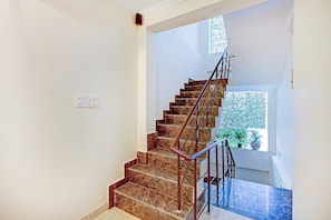 A staircase with marble steps and metal railings, leading to a landing with a window and a potted plant. - Hotel O Sky In Near By Sector 62 (Ghaziabad)