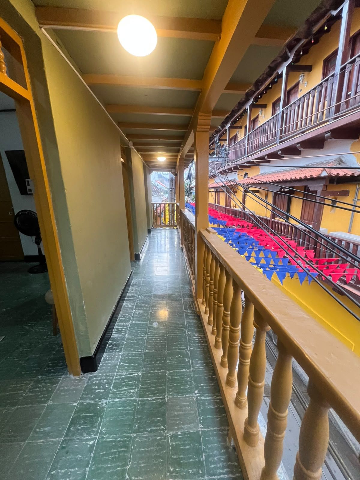 Un pasillo con barandilla de madera, piso de baldosas y vistas a un edificio con balcones.