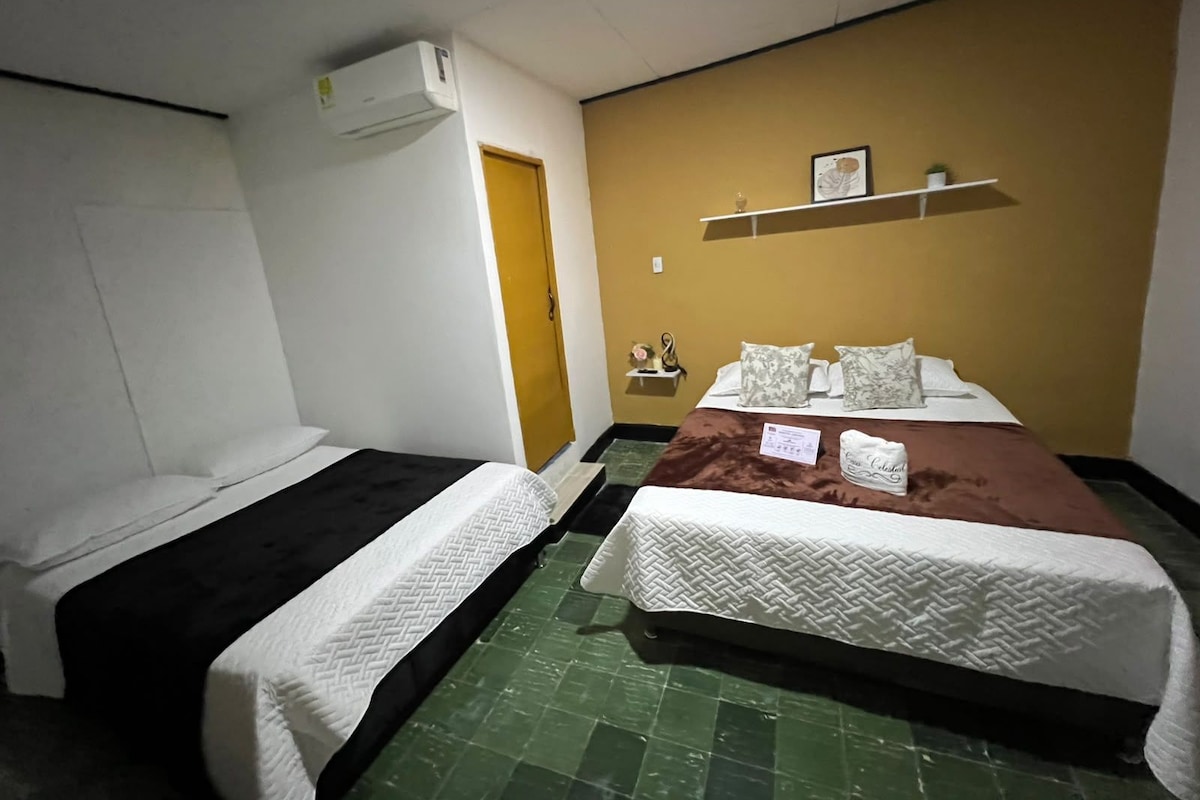 A hotel room with two beds, a wardrobe, a shelf with decorative items, and a green tiled floor.