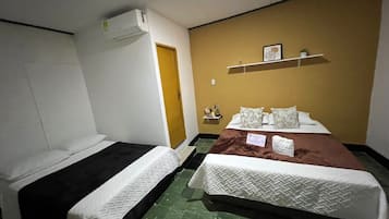 Habitación de hotel con dos camas, un armario, una repisa con adornos y piso de baldosas verdes.