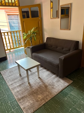 A room with a brown sofa, a small white table, a patterned rug, and a potted plant. - Casa Celestial (Cartagena)