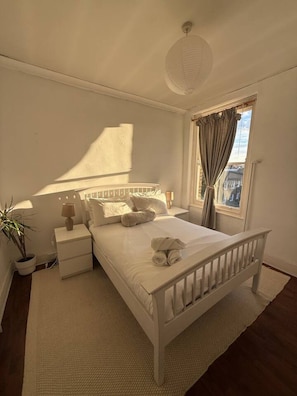 A bedroom with a single bed, bedside tables, a nightstand, a lamp, a potted plant, and a window with curtains. - Sunny 2-Bed Triplex with Private Terrace (Greater London)