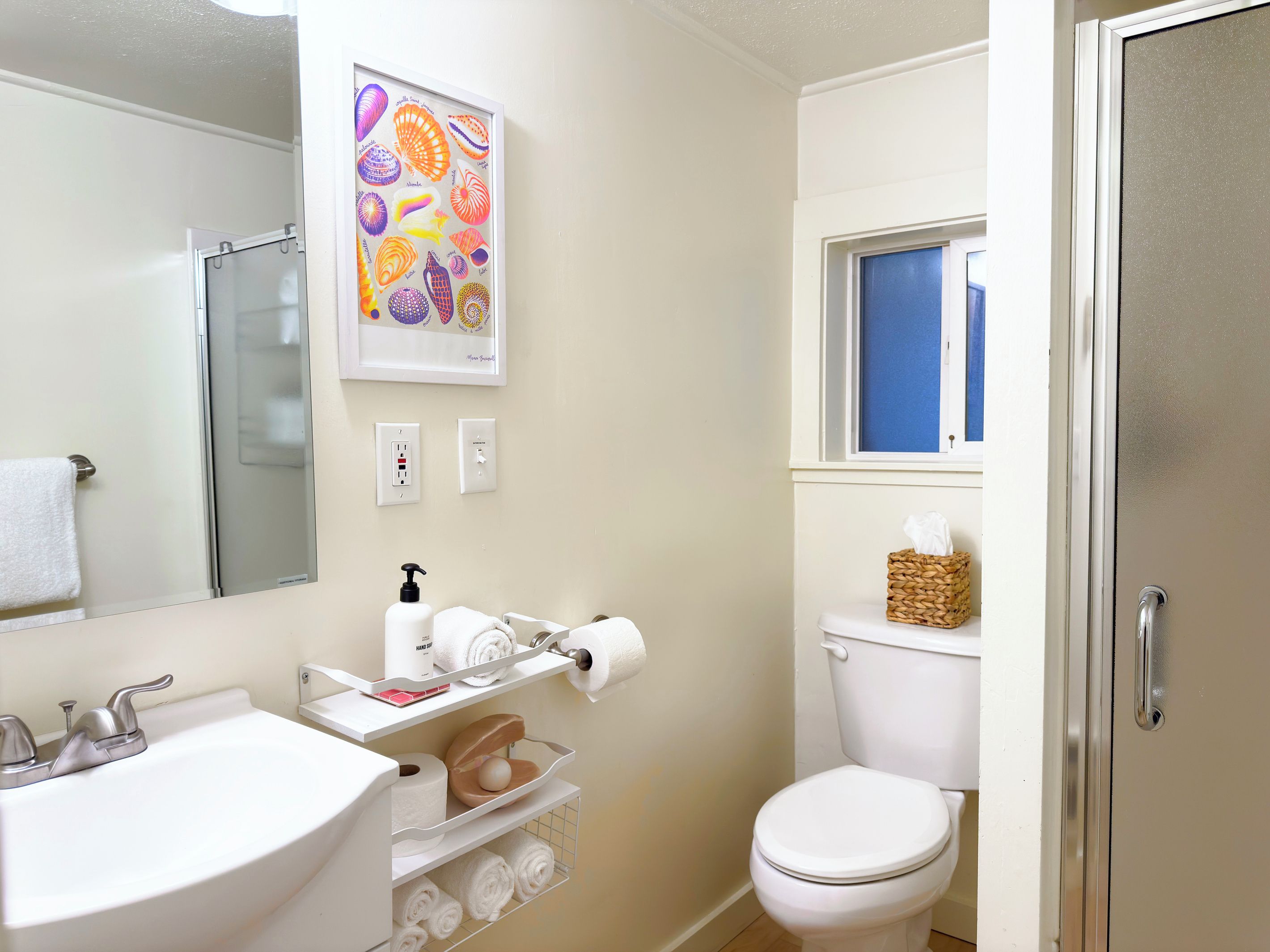A bathroom with a sink, toilet, and a framed artwork above the mirror.