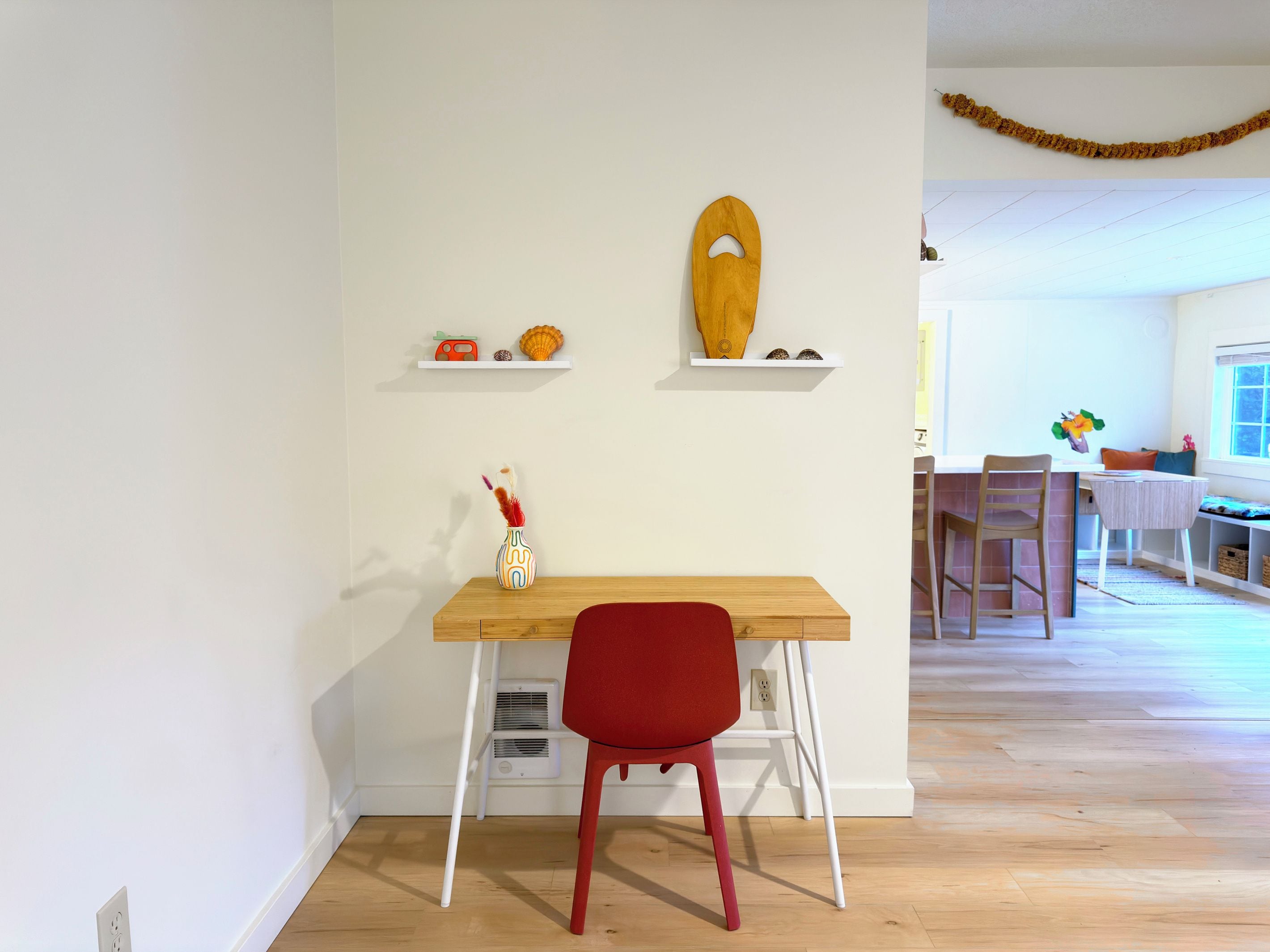 A room with a wooden desk, a red chair, and a white wall with decorative items.