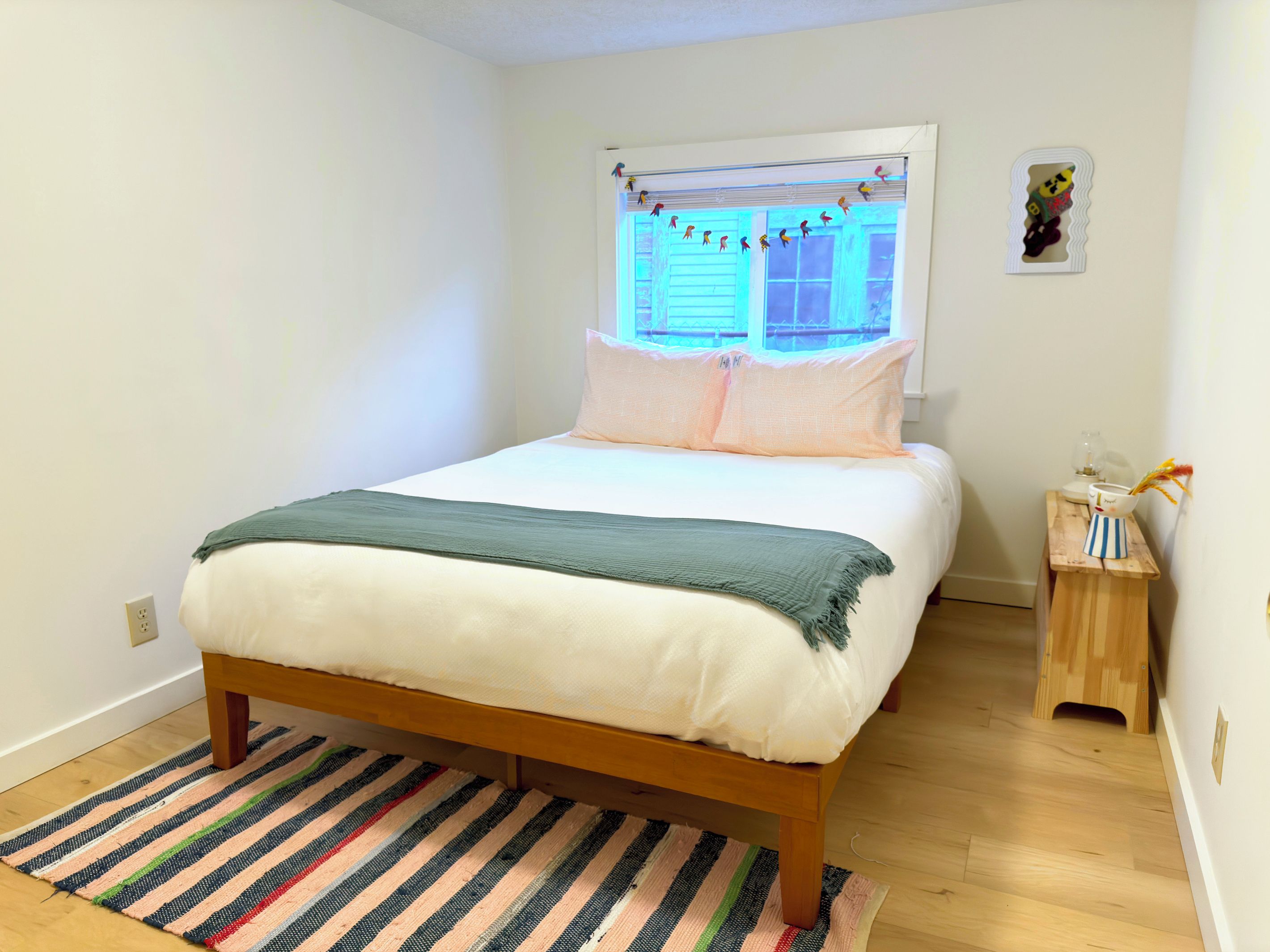 A bedroom with a bed, a window with curtains, a bedside table, and a small wooden nightstand.