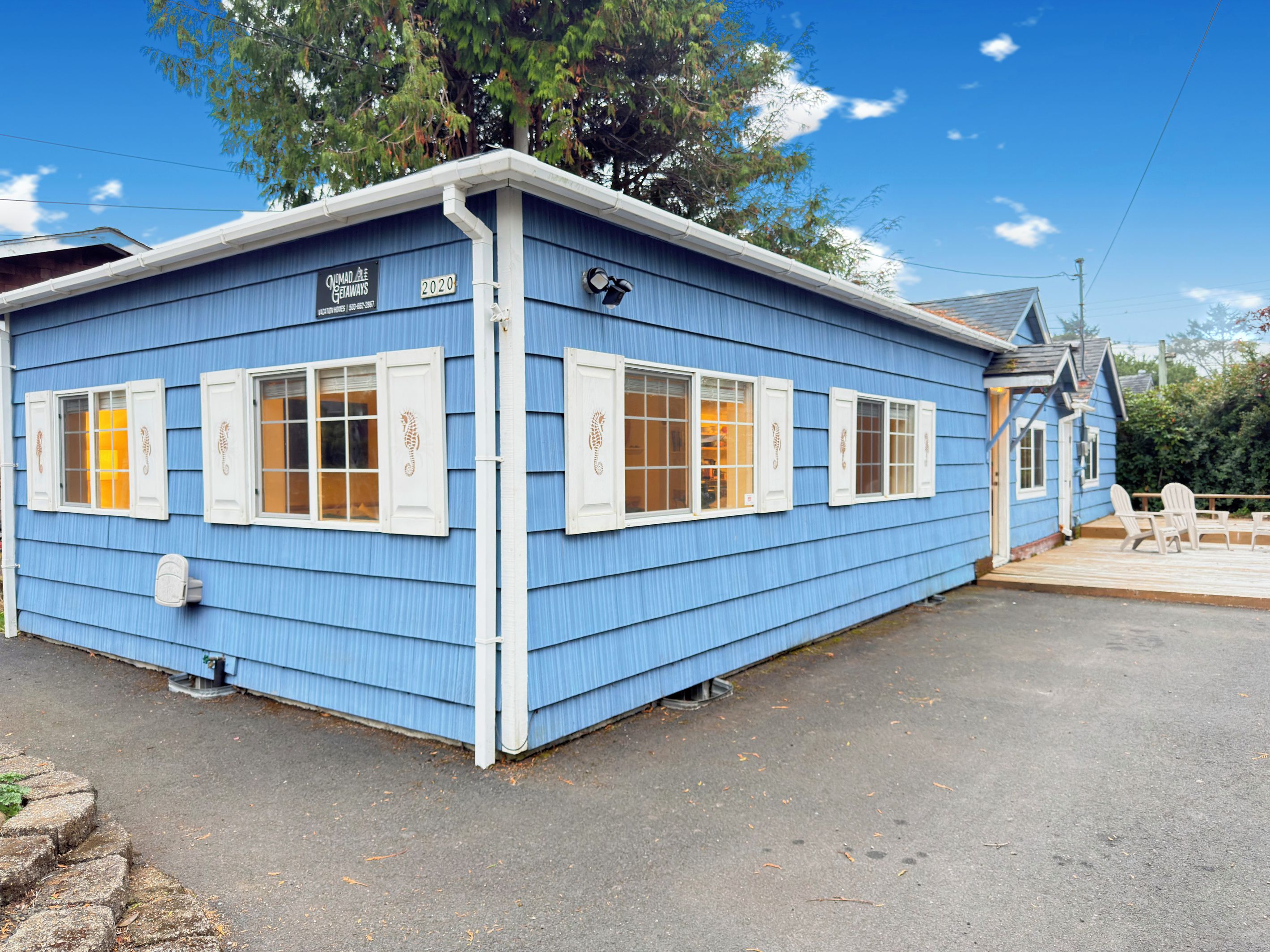 A blue building with white shutters, a sign with the year 2020, and a small deck area with chairs.