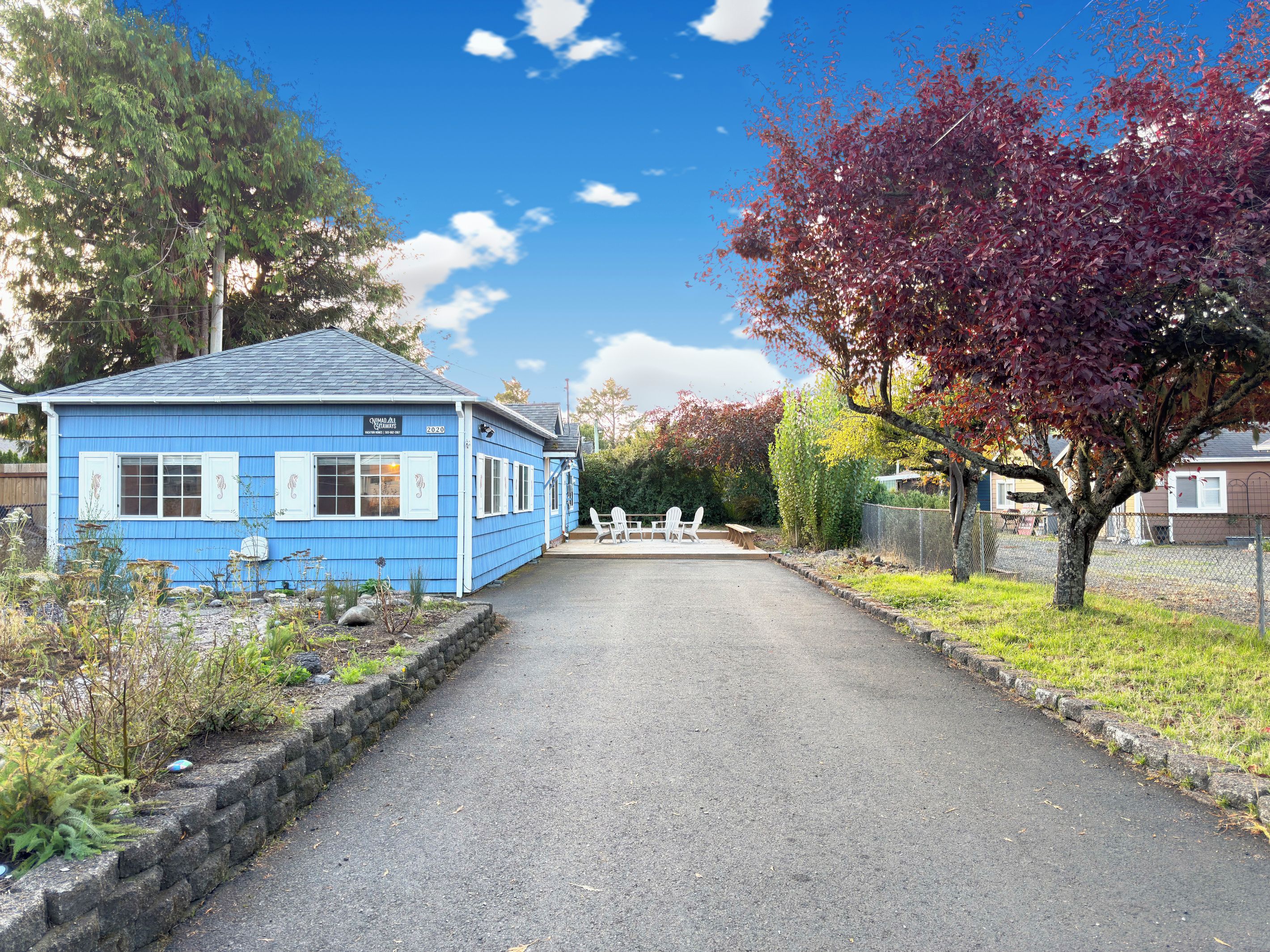 A blue building with a sign, a paved driveway, and outdoor seating.