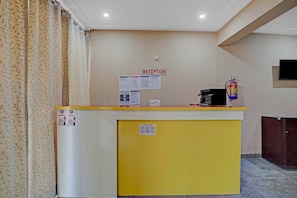 A reception desk with a 'RECEPTION' sign, a fire extinguisher, and a wall-mounted television. - Hotel O AKKI RESIDENCY (Noida)