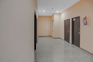 A hallway with a fire extinguisher mounted on the wall, a door on the right, and a door on the left. - Hotel O AKKI RESIDENCY (Noida)
