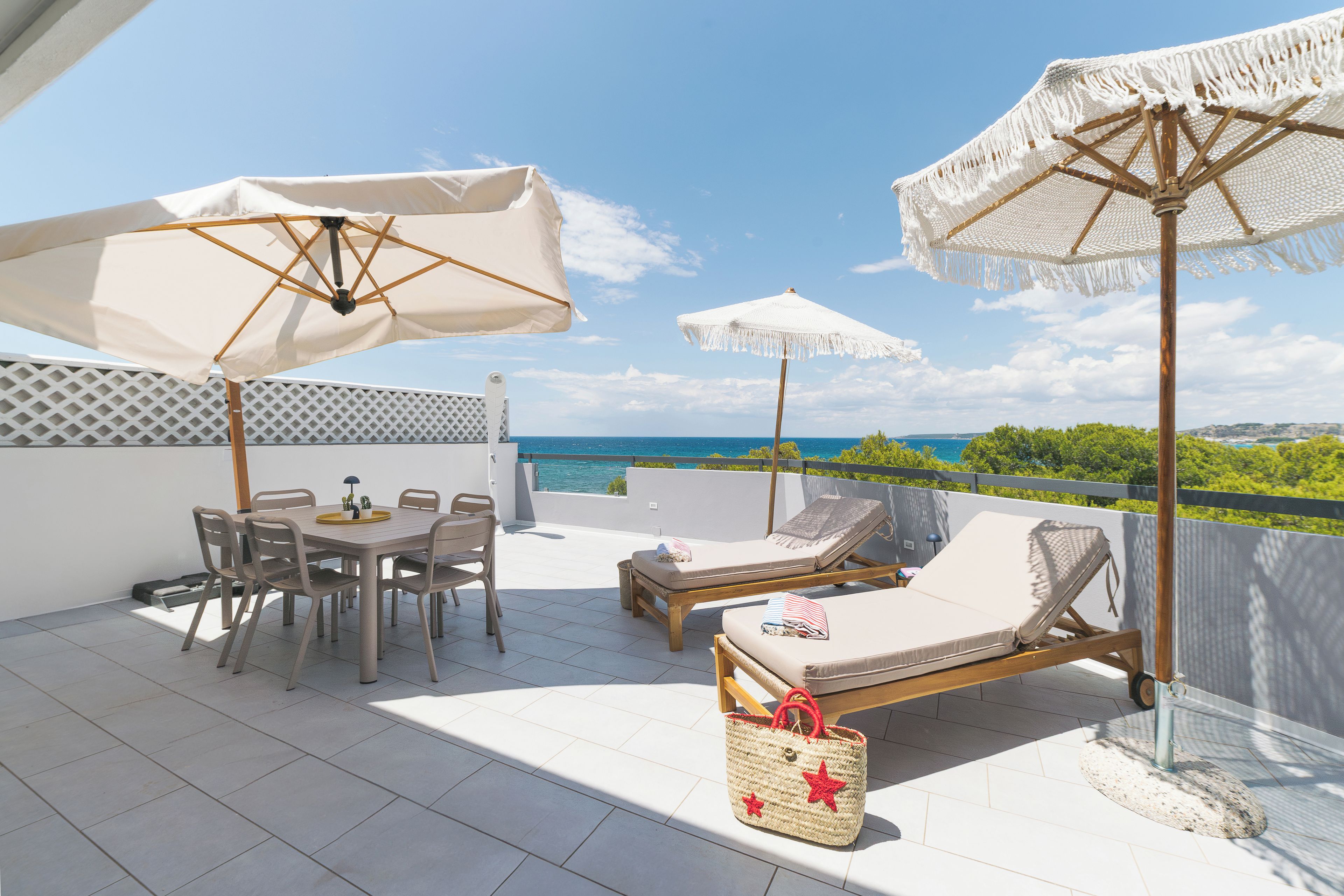 A terrace with a table and chairs, two lounge chairs, and two umbrellas.