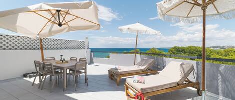 A terrace with a table and chairs, two lounge chairs, and two umbrellas.
