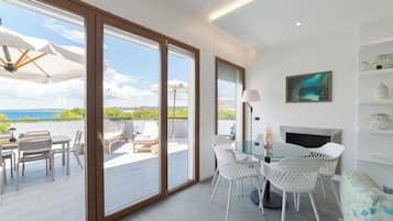 Un interno moderno con una porta in vetro che dà su un'area salotto esterna con vista sul mare.