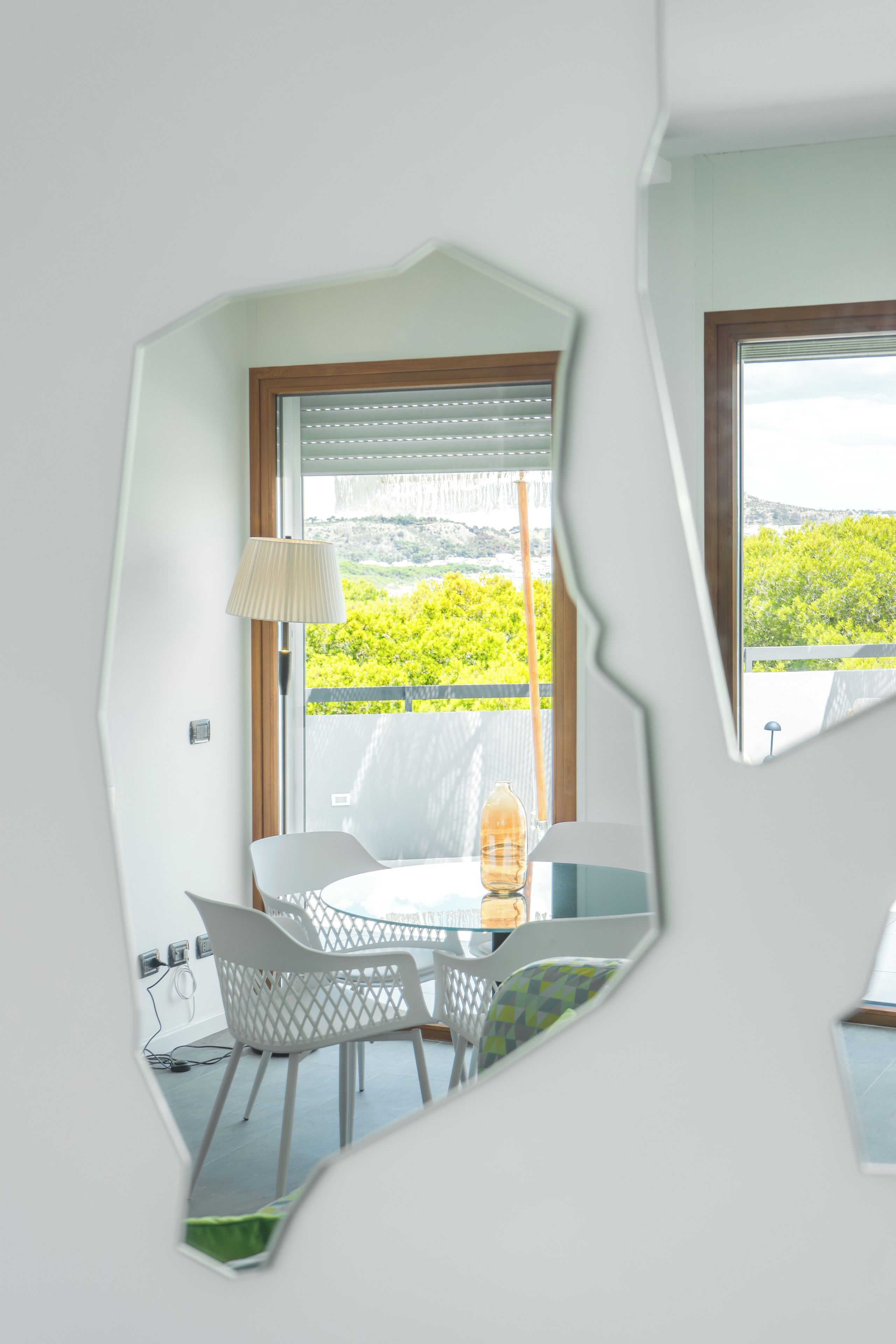 Une pièce avec une table et des chaises, une fenêtre donnant sur un paysage verdoyant et des collines, et une lampe.