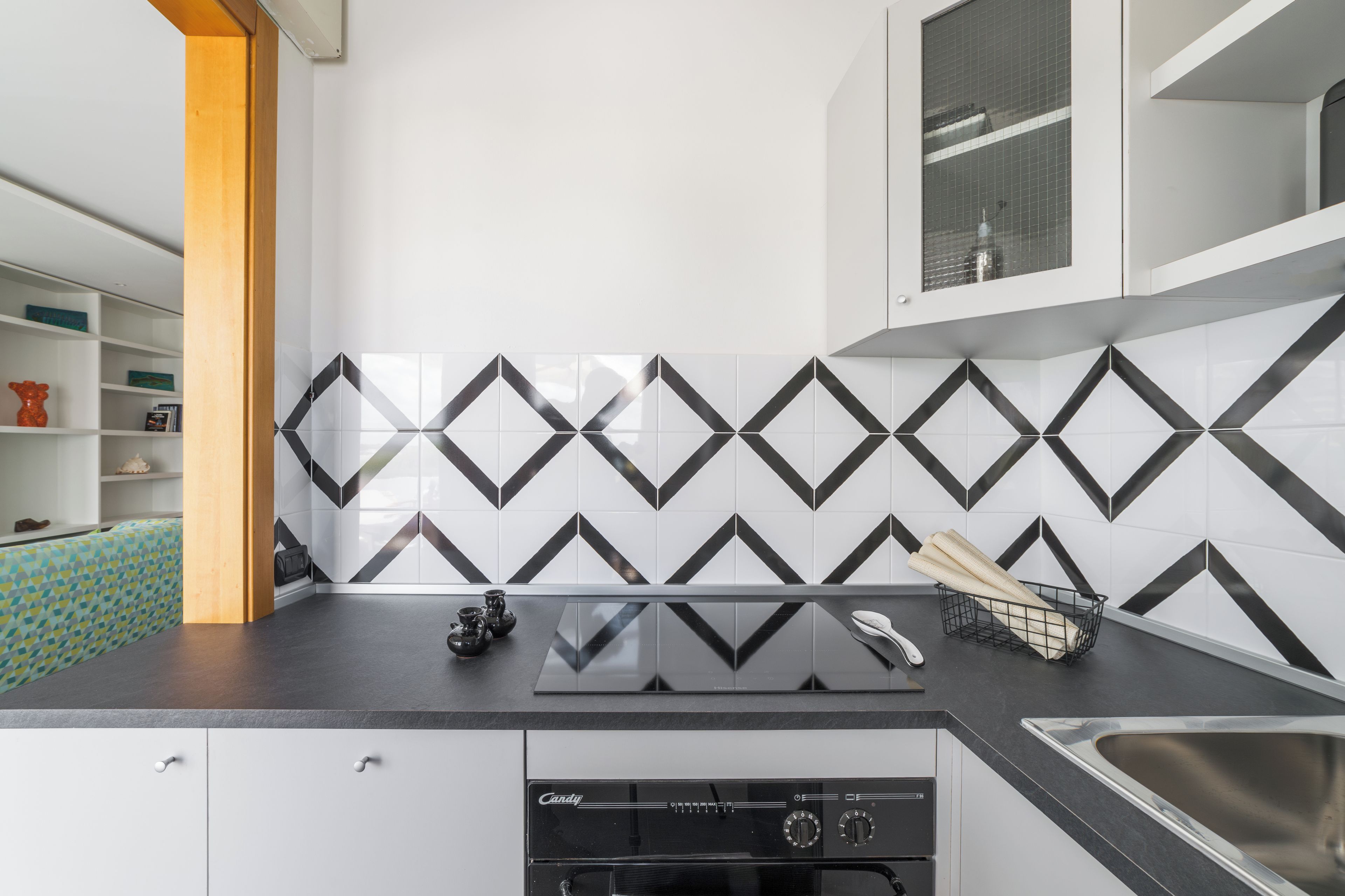 Une cuisine avec un dosseret en carreaux noirs et blancs disposés en chevron, un plan de travail noir et un lave-vaisselle.