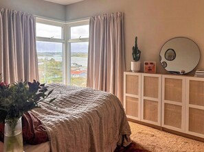 A bedroom with a large window, a bed with a patterned bedspread, a cactus on a bedside table, and a round mirror on the wall. - Architect-designed villa with sea views near Tjörn (Stenungsund)