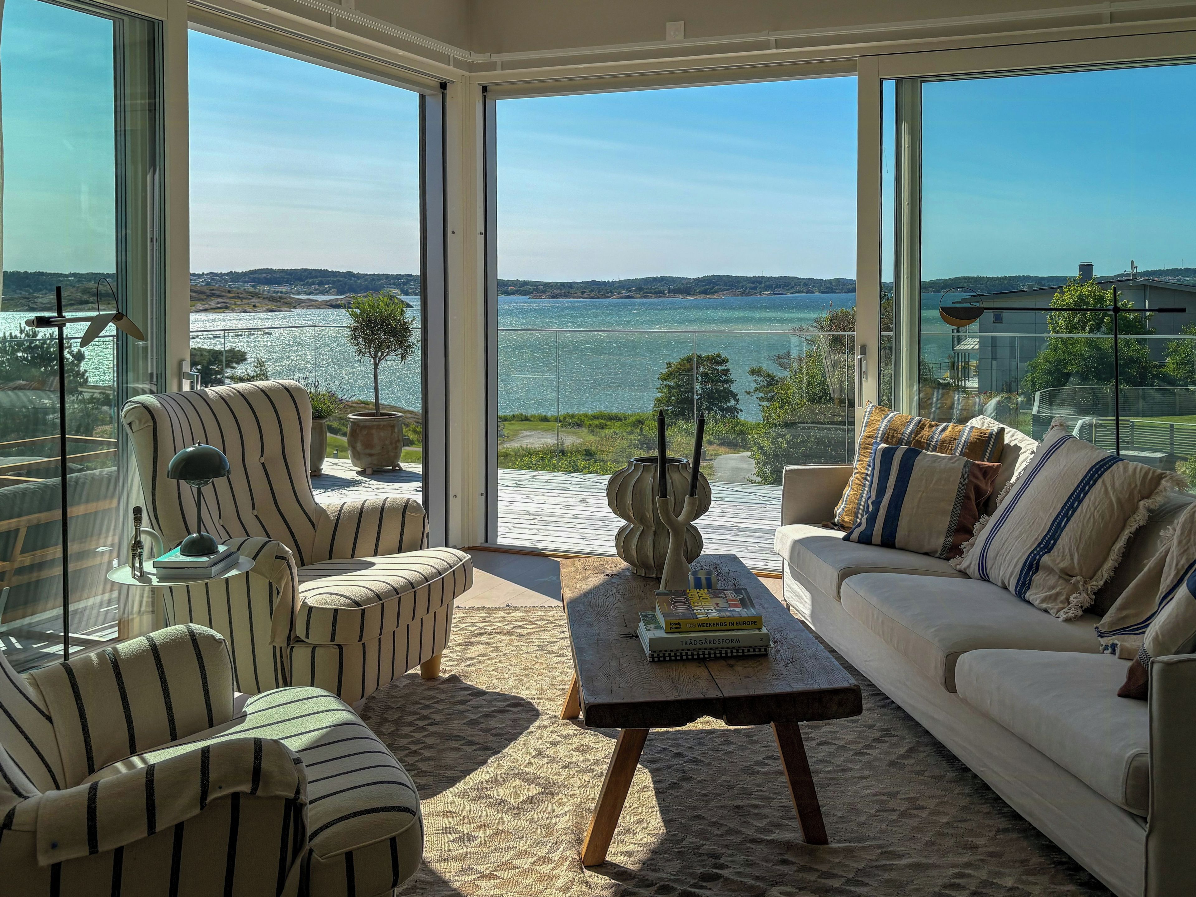 Een moderne woonkamer met een grote glazen deur die uitkomt op een balkon met uitzicht op een waterpartij.