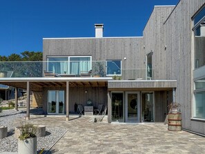 A modern two-story building with a wooden exterior, large windows, and a covered outdoor seating area. - Architect-designed villa with sea views near Tjörn (Stenungsund)