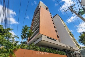 A multi-story building with a prominent orange facade, a visible entrance with a sign, and a clear blue sky in the background. - Studio in Condo. w/ Pool in Barra Eub0704 (Salvador)